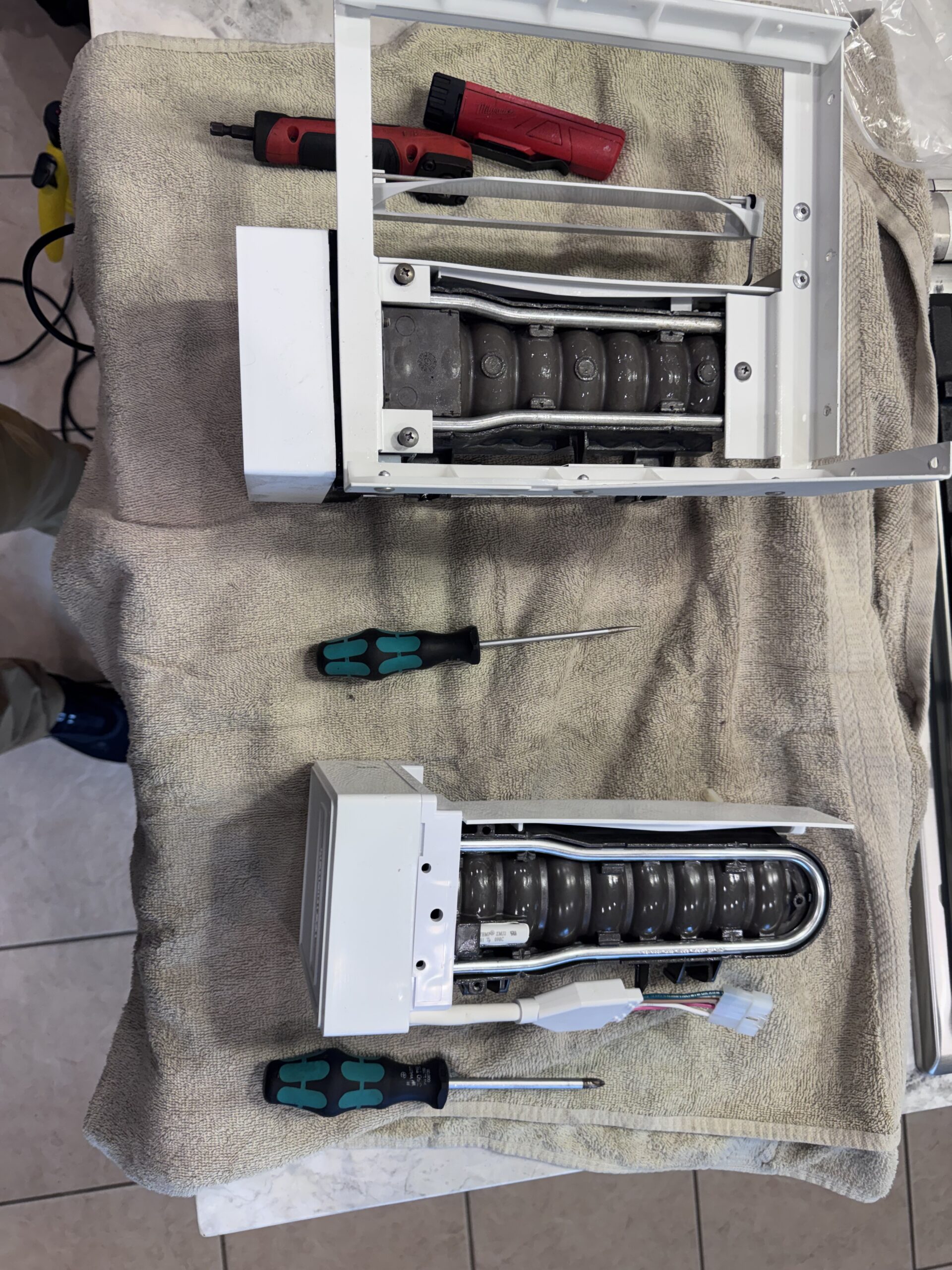 Old and new Sub-Zero ice maker assemblies during replacement